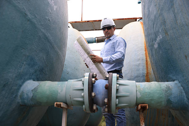 istock A construction professional wearing a hard hat and sunglasses work with walkie-talkie and blueprint drawing at site of large  water tanks and valve. emphasizing communication and teamwork in an industrial environment 2250748105