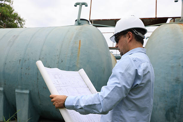 istock A construction professional or senior engineer wearing a hard hat and sunglasses examines blueprints while standing between large water tanks 2250748150