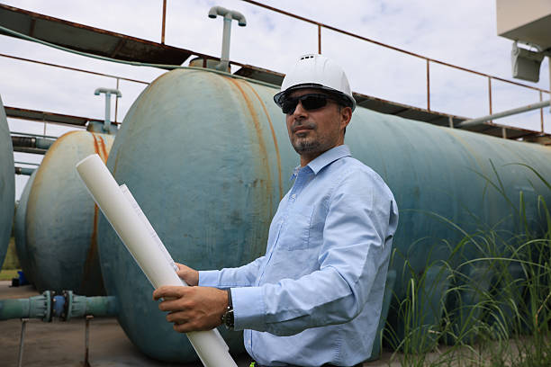 istock A construction professional or senior engineer wearing a hard hat and sunglasses examines blueprints while standing between large water tanks 2250748170