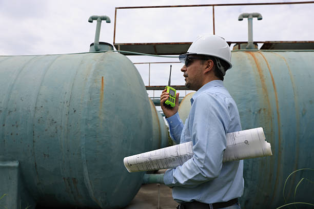 istock A construction professional or senior engineer wearing a hard hat and sunglasses examines blueprints while standing between large water tanks 2250748171