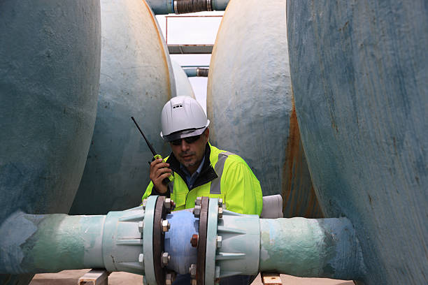 istock A construction professional wearing a hard hat and sunglasses work with walkie-talkie and blueprint drawing at site of large  water tanks and valve. emphasizing communication and teamwork in an industrial environment 2250748271