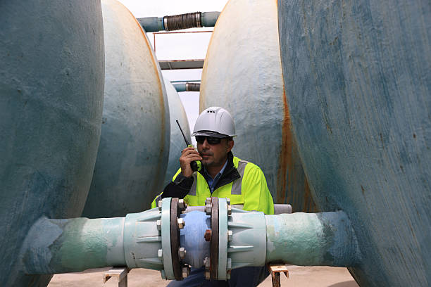istock A construction professional wearing a hard hat and sunglasses work with walkie-talkie and blueprint drawing at site of large  water tanks and valve. emphasizing communication and teamwork in an industrial environment 2250748845