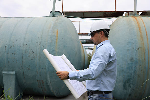istock A construction professional or senior engineer wearing a hard hat and sunglasses examines blueprints while standing between large water tanks 2250748851