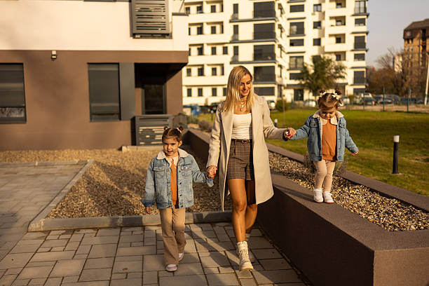 istock Mother Walks With Two Daughters In Denim Jackets Along Modern Apartment Complex Path 2250755994