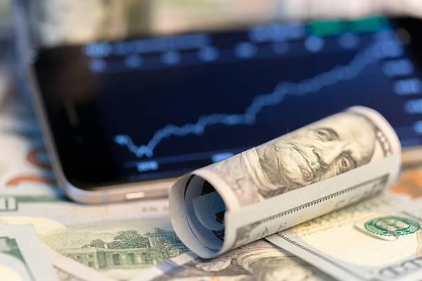 istock Financial growth visualization with rolled currency and smartphone displaying market trends 2250758286