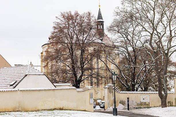 Prague, czech republic - november 24, 2025: strahov monastery church with surrounding trees and walls covered in light november snow in hradcany