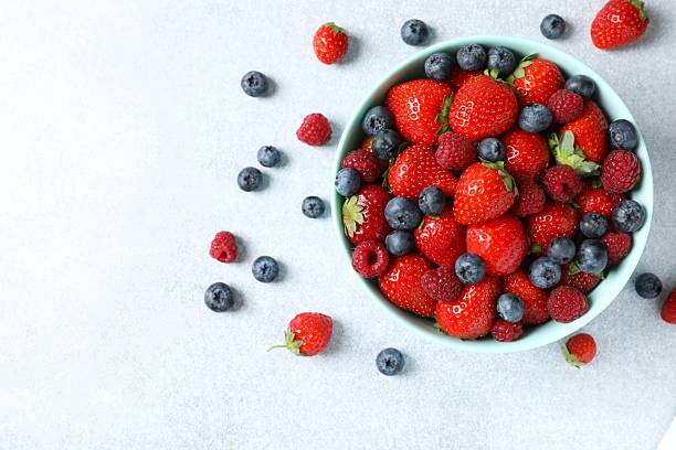 istock Different fresh ripe berries in bowl on wooden table, top view 2250762660