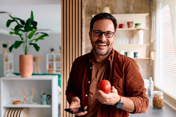 istock Happy man holding apple and phone in kitchen 2250777594