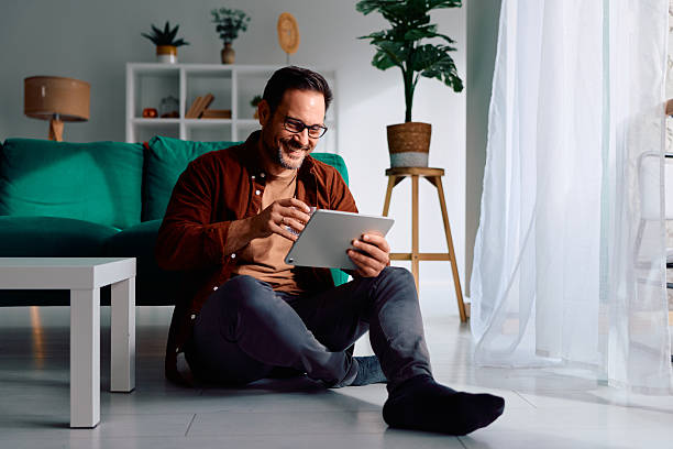 istock Smiling man using digital tablet sitting on floor at home 2250777755