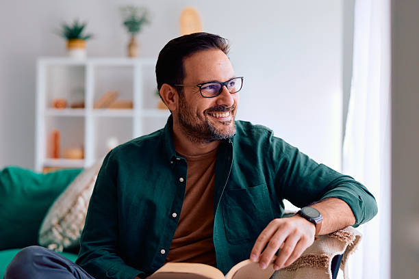 istock Smiling man relaxing at home reading book 2250779100
