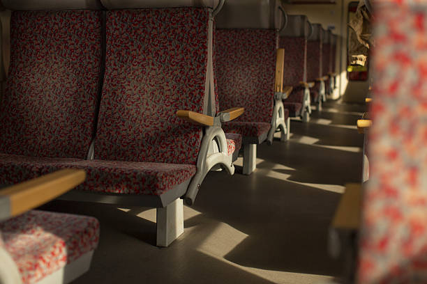 empty train carriage patterned seats bathed in golden light, wooden armrests and long aisle after rush hour maintenance crew