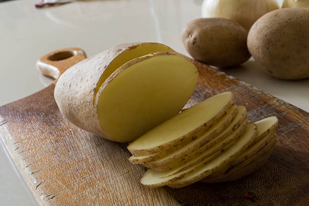 The close-up view of a woman's hand is moving sliced ​​potatoes into a glass bowl