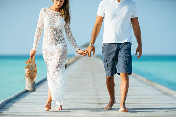 Young couple walking holding hands along jetty at Dhiffushi Holiday island, South Ari atoll, Maldives. Model and Property released. Hi resolution photo.