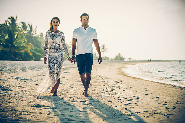 Young couple walking along beach holding hands at Dhiffushi Holiday island, South Ari atoll, Maldives. Model and Property released. Hi resolution photo.