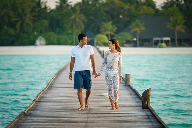Young couple walking holding hands along jetty at Dhiffushi Holiday island, South Ari atoll, Maldives. Model and Property released. Hi resolution photo.