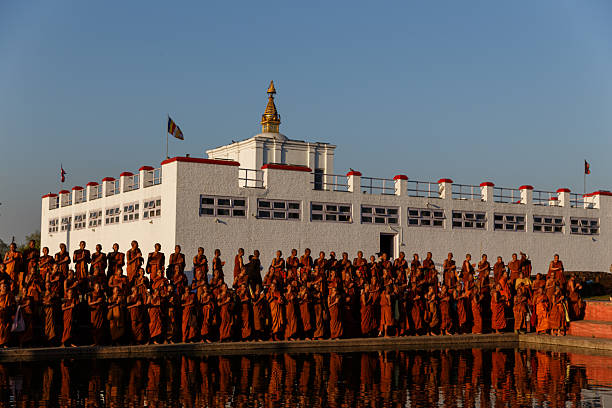 A large group of Buddhist monks in traditional orange robes stand together during a ceremonial event at the Maya Devi Temple in Lumbini, Nepal, the birthplace of Buddha. Editorial image depicting Buddhist culture and religious practices.