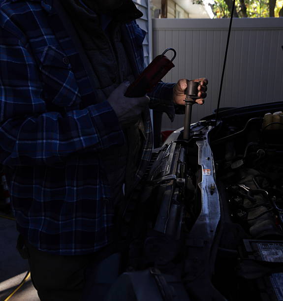 A senior man holds a work light as he starts a DIY vehicle repair in a home driveway in Metro Vancouver.