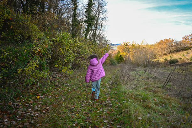 Child walking a dirt path with fall trees, pointing towards distant hills