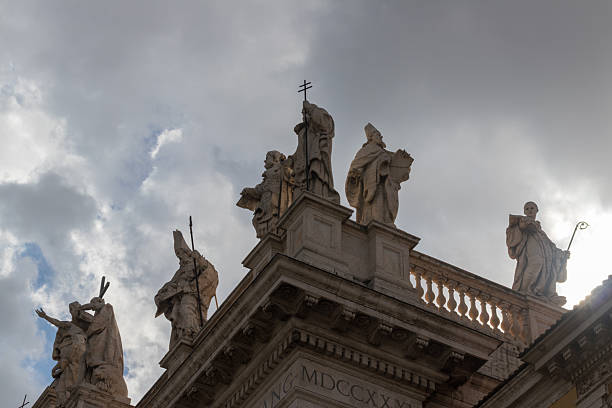 Historic stone statues atop an architectural building with a cloudy sky, symbolizing history and culture.