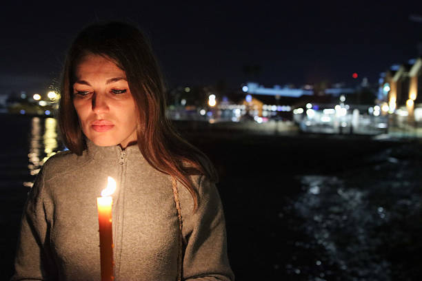 A woman stands on the riverbank at night, holding an old lantern