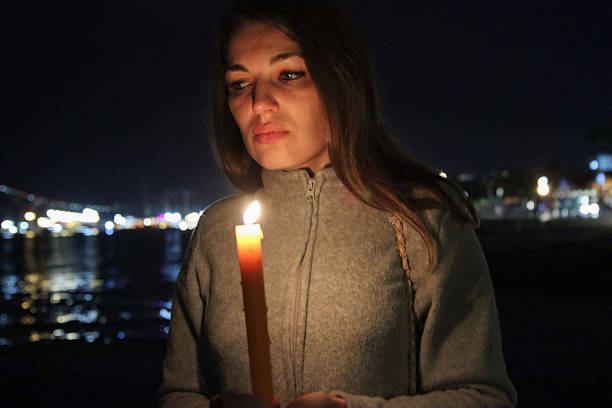 Woman standing outdoors at night, holding a burning candle, reflecting on life's moments