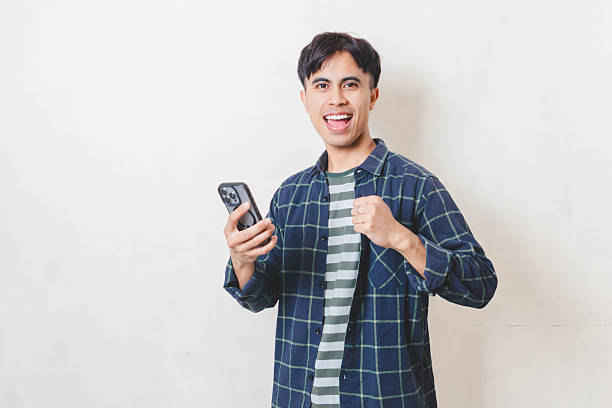 istock Cheerful young man celebrating a positive result while holding a smartphone, showing excitement and success in a bright indoor setting. 2250817280