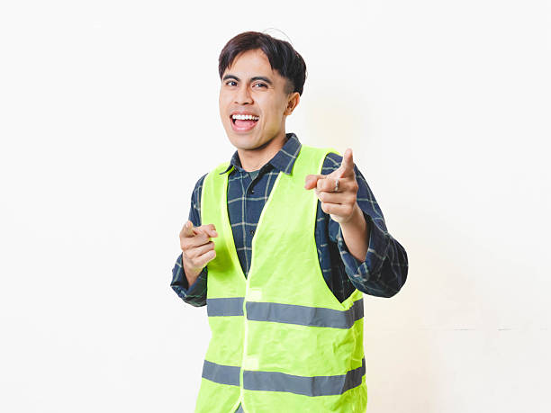 istock Smiling construction worker in a safety vest pointing forward with a cheerful and playful expression, isolated on white background. 2250817653