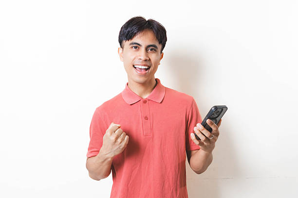 istock Man celebrating success while holding a smartphone, showing excitement and happiness with a cheerful expression on a clean background. 2250823718