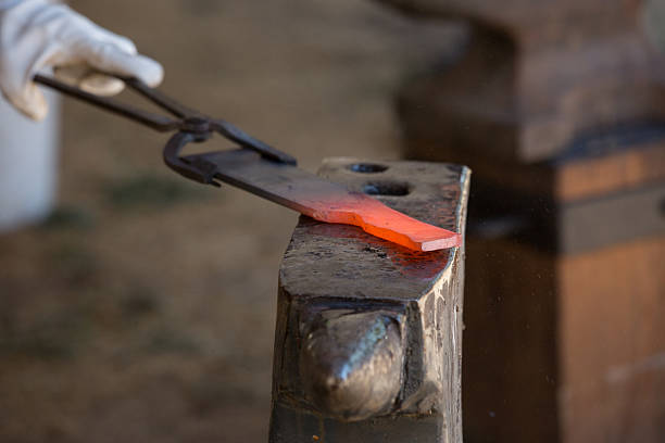 close up of a blacksmith holding a red-hot piece of metal with tongs