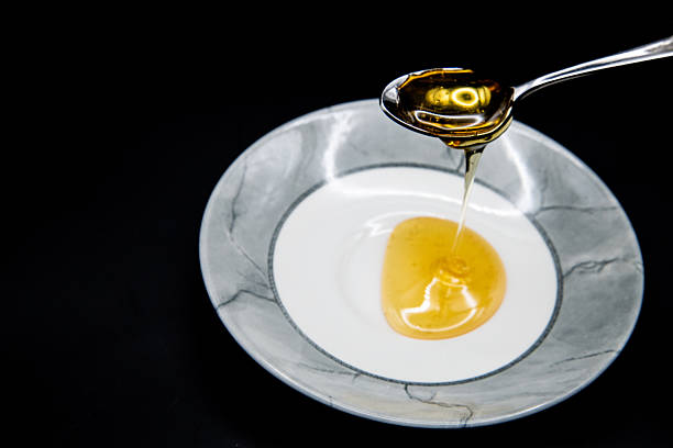 istock Honey Dripping from Spoon into Bowl on Black Background 2250825807