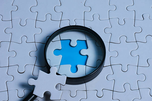 istock Magnifying glass focusing on the missing gap of a white puzzle, with the missing piece placed on the magnifying glass 2250828779