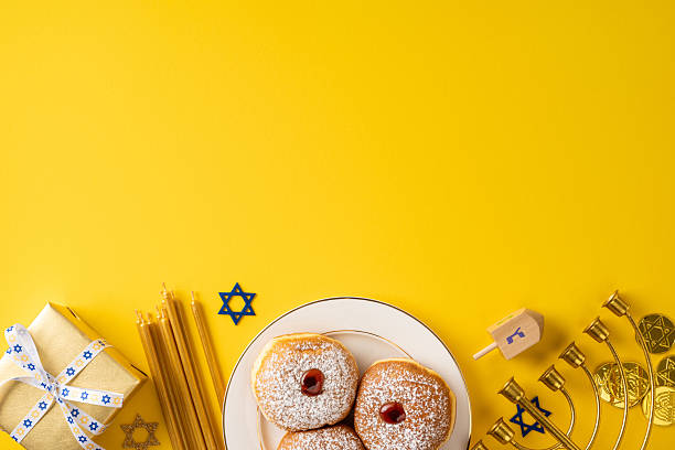 istock A festive Hanukkah scene features sufganiyah donuts, a lit menorah, a spinning dreidel, and a gift on a sunny yellow backdrop. Warm, celebratory mood suitable for greeting cards and seasonal campaigns 2250828784