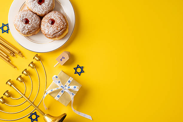 istock Rich Hanukkah scene featuring a menorah, dreidel, gift box, ribbon and powdered donuts on a bold yellow backdrop. Festive, warm, and celebratory 2250828792