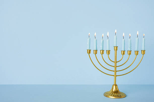 istock A brass menorah stands on a blue surface with nine lit candles, capturing a warm Hanukkah moment ideal for holiday greeting, tradition, and festive lighting in a contemporary home setting 2250828817
