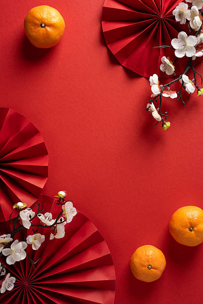 Vibrant vertical Chinese New Year scene featuring bright red fans, mandarins, and delicate white blossoms arranged on a bold red backdrop