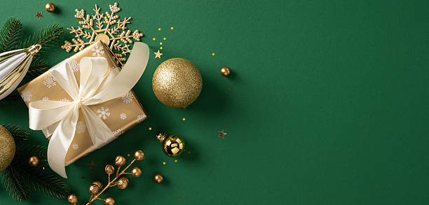 istock A gold wrapped gift sits beside a gold ornament and delicate snowflake accent, set on a deep green banner to evoke festive warmth and Christmas season charm for stock use 2250829172
