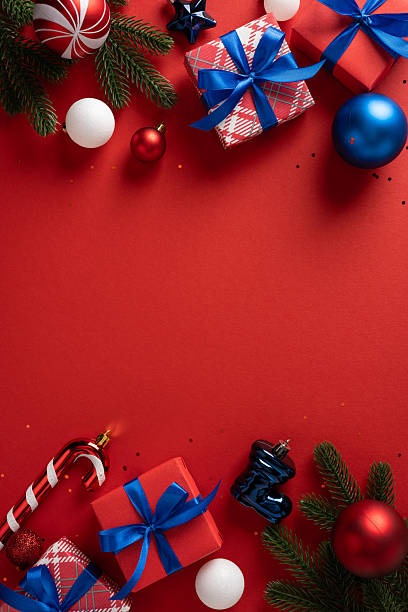 istock A vertical festive red background features wrapped gifts with blue ribbons, ornaments, a candy cane, and evergreen branches, creating a cheerful holiday scene 2250829176