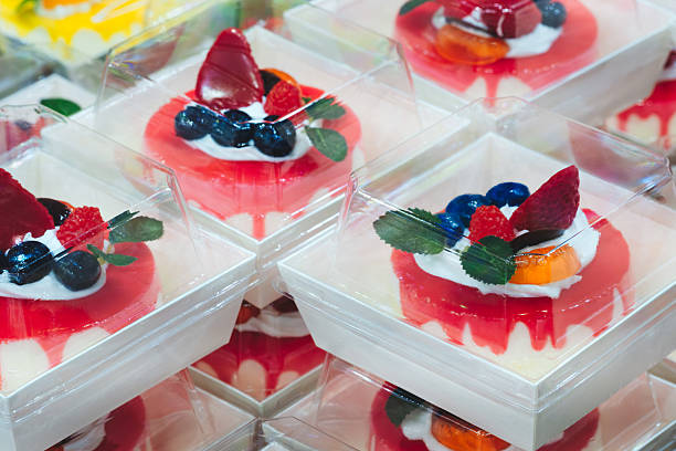 A stack of dessert boxes with a red cake in the middle.  cake is topped with strawberries and blueberries