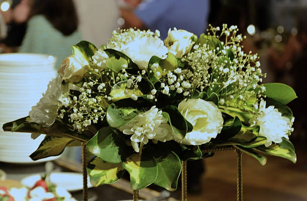 A floral arrangement featuring baby's breath (Gypsophila paniculata), white chrysanthemum (Chrysanthemum morifolium), white roses (Rosa × alba), and green foliage on the dining table.