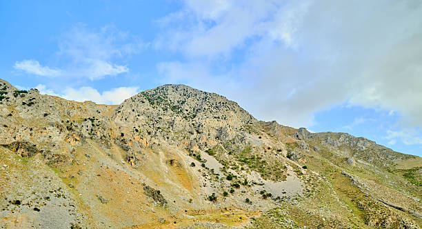 Crete, Greece presents a dramatic rocky mountain landscape with exposed slopes and sparse vegetation under a bright blue sky. This natural, rugged terrain evokes adventure, outdoor exploration, and travel inspiration, capturing geological textures, earthy tones, and expansive horizons perfect for nature and landscape stock uses.