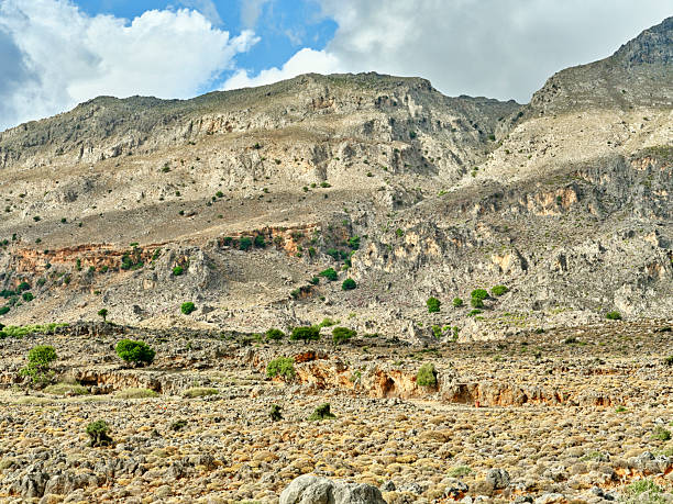 Crete landscape in Greece showcases rugged mountains, rocky hills, and an arid hillside beneath a bright blue sky with white clouds. This natural outdoor scene highlights Greek terrain and scenery, perfect for travel, nature, tourism, and adventure stock projects celebrating Crete and Greece.