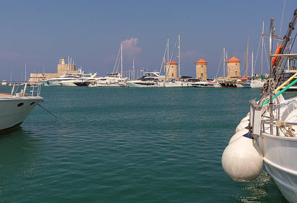View of yachts, medieval windmills and Fort Saint Nicholas at Mandraki harbor in Rhodes, Greece