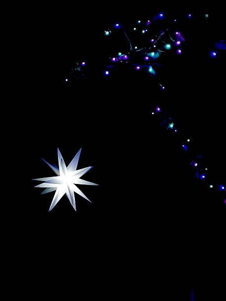 Illuminated star shaped paper lantern floating against black background with space for copy beneath colorful lights.