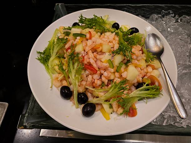 Fresh and vibrant close-up shot of a shrimp and fruit salad, featuring diced prawns, crisp lettuce (frisée), black olives, and various chopped fruits and vegetables.