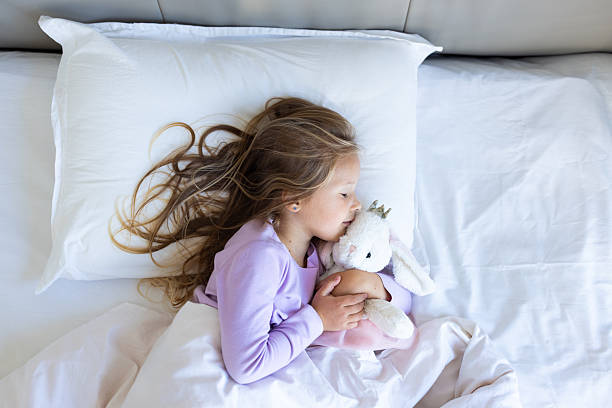 istock Young girl sleeping in bed while hugging a stuffed animal toy 2250850382