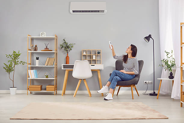 istock Young satisfied woman at home adjusts air conditioning in room using remote control. 2250858564