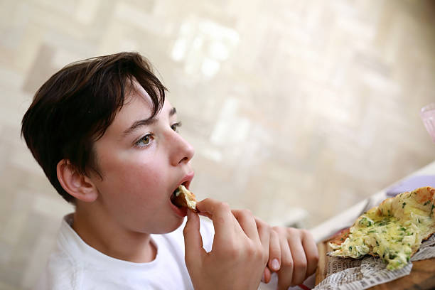 istock Boy eating slice of cheesy garlic bread 2250868379