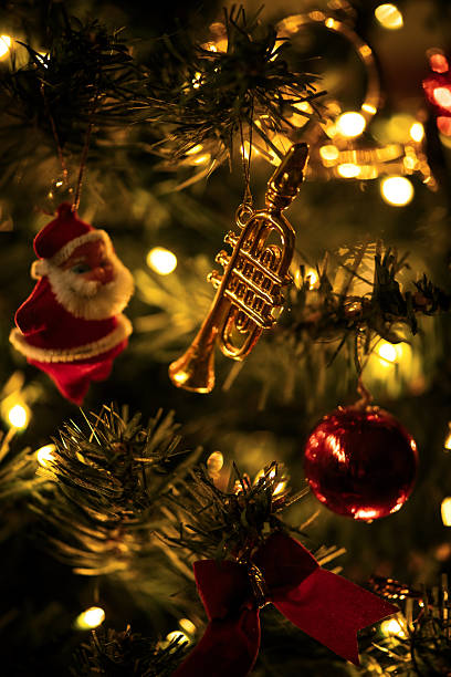 A warm and intimate macro captures the charm of a Christmas tree decorated with nostalgic ornaments. A tiny Santa figure, a golden trumpet, a deep red bauble, and a velvet bow sit among softly illuminated branches. The golden fairy lights glow gently, creating a cozy, timeless atmosphere.