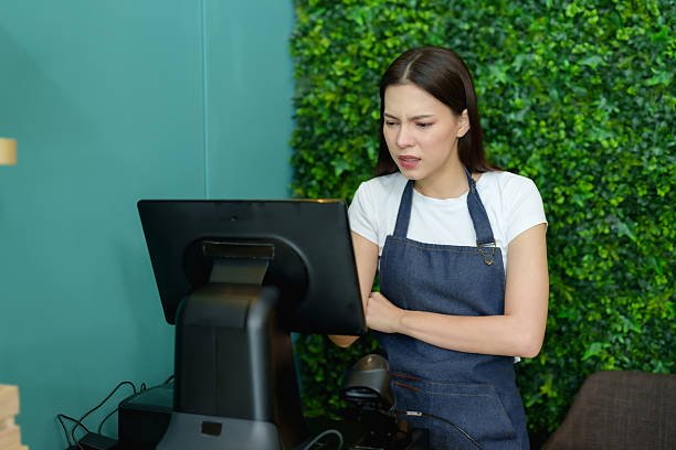 istock Female entrepreneur in apron crossing arms staring at POS screen while thinking about fruit shop setup preparing digital checkout system before starting small local business 2250875869