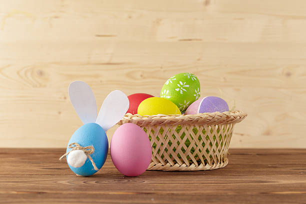 istock Colorful Easter eggs and a bunny made of egg standing beside a basket on a wooden table 2250876758